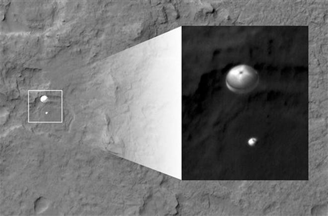 In this image released by NASA/JPL-Caltech/Univ. of Arizona, NASA's Curiosity rover and its parachute, left, descend to the Martian surface on Sunday. The high-resolution Imaging Science Experiment (HiRISE) camera captured this image of Curiosity while the orbiter was listening to transmissions from the rover. The inset image is a cutout of the rover stretched to avoid saturation. The rover is descending toward the etched plains just north of the sand dunes that fringe "Mt. Sharp." (AP Photo/NASA/JPL-Caltech/Univ. of Arizona)