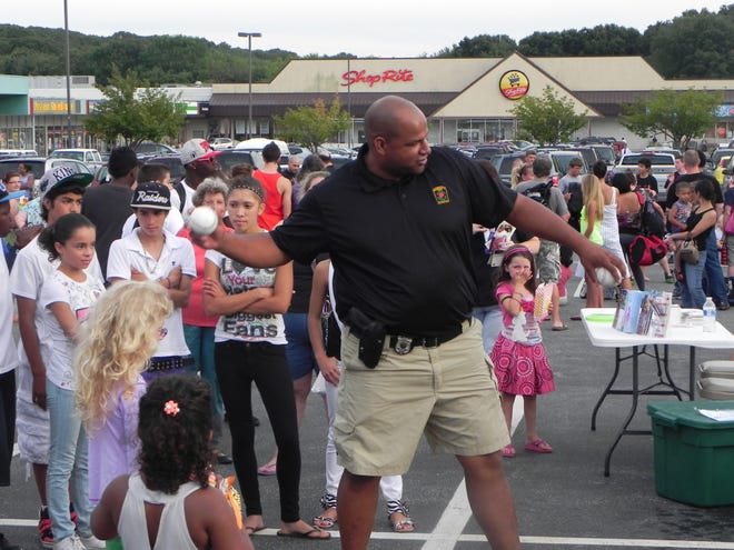 Norwich Police Officer Anthony Gomes demonstrates how to toss a softball at the dunk tank during Tuesday's National Night Out Against Crime in the Shop Rite parking lot in Norwich.