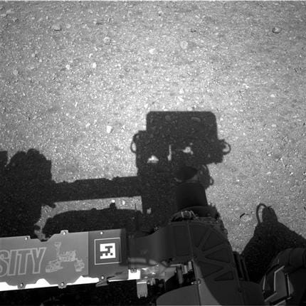 This image released by NASA on Wednesday, Aug. 8, 2012, shows the edge of NASA's Curiosity rover, showing the shadow of the rover's now-upright mast in the center, and the arm's shadow at left. The navigation camera is used to help find the sun -- information that is needed for locating, and communicating, with Earth.
