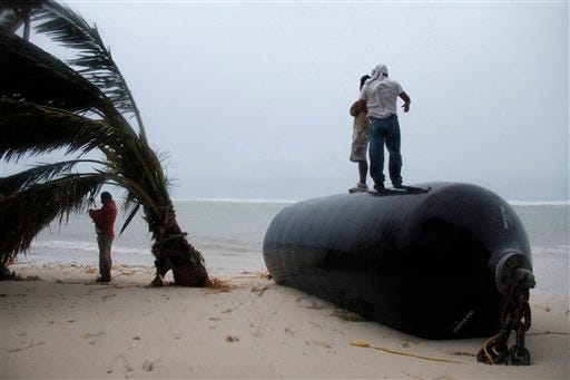 Two men stand on top of a marine fender that was ripped from a dock after Hurricane Ernesto made landfall overnight in Mahahual, near Chetumal, Mexico, Wednesday, Aug. 8, 2012.