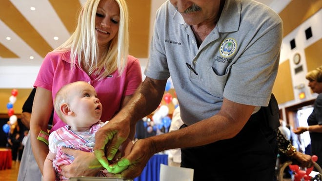 J'Anine Benzing, left, holds her 8-month-old daughter J'Aclyn as she is fingerprinted by Palm Beach Police crime scene technician Bill Waterfield Tuesday at Palm Beach's National Night Out Against Crime.