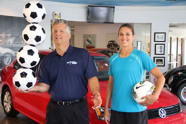 Olympic gold medal winner Carli Lloyd watches as Gus Staino, managing partner of Burlington Volkswagen, holds a string of soccer balls in the dealership showroom where Lloyd made a commercial that airs on cable television stations.