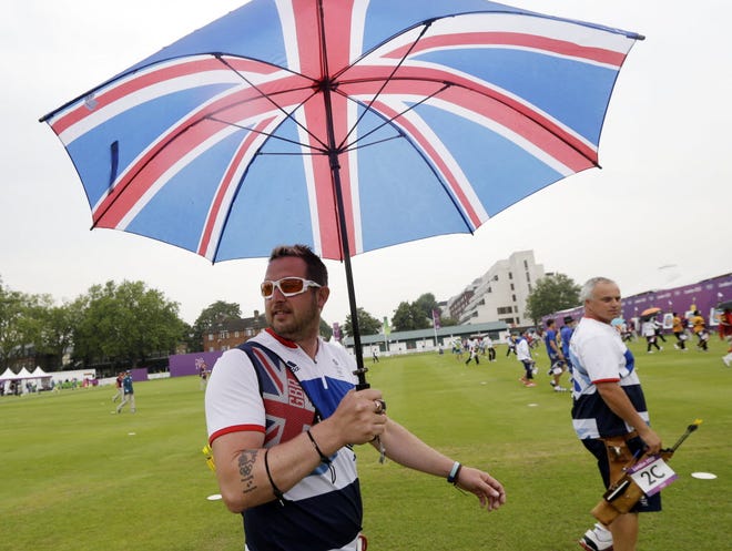 Britain's Laurence Godfrey shields from the rain next to teammate Simon Terry during an individual ranking round at the 2012 Summer Olympics in London. Wet weather this summer in London has forced retailers to discount unsold summer merchandise.