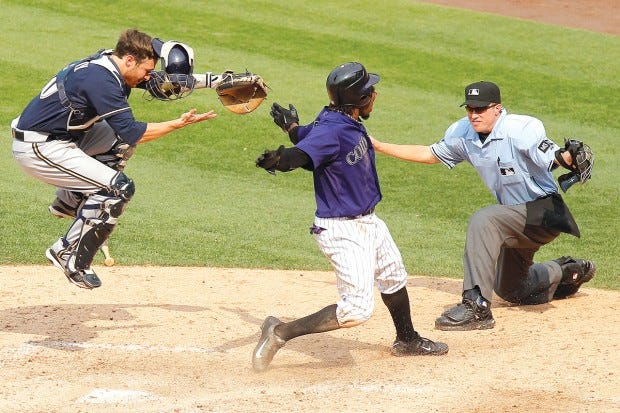 The Rockies' Eric Young Jr. scores the winning run in the bottom of the ninth inning, beating the throw to Brewers catcher Jonathan Lucroy (left) as umpire Cory Blaser (right) makes the call. (AP PHOTO/BARRY GUTIERREZ)