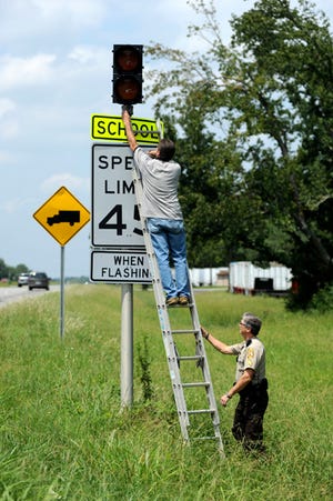 Sgt. Lanny Handy, the school resource officer coordinator for the Etowah County Sheriff's Office, steadies the ladder and watches out for traffic as Roger Lay with the Etowah County Schools maintenance department checks on a school speed limit sign August 16, 2012, in Etowah County, Ala. The traffic patterns at Carlisle School will be changing because of the influx of new students.