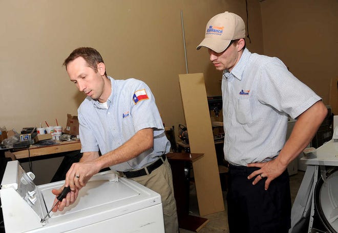 Jack Klaus, left, owner of Amarillo Appliance, shows field technician Trey Stone how to take apart a dryer Thursday at the store's shop.