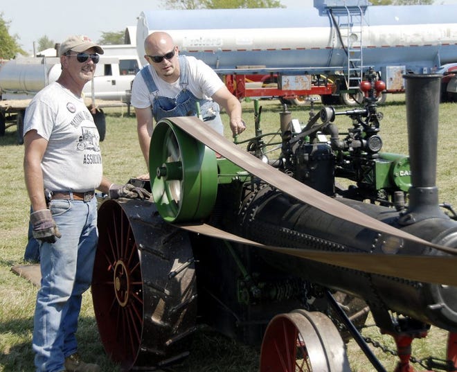 Jim Haley, owner of a half-scale model 65 hp Case watches as Mitch Bailey prepares his steam engine for threshing.