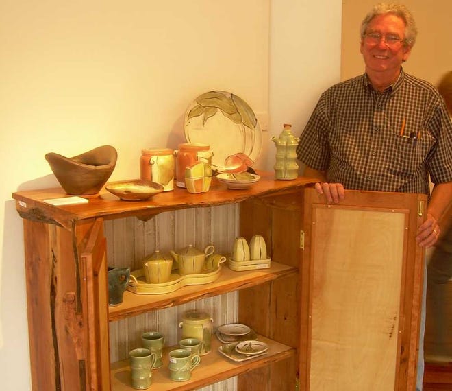 Watkinsville wood artist Larry McDougald stands next to the cabinet he built that is full of pottery made by Isabell Daniel of Farmington.