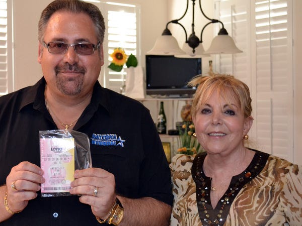 Leo and Kitsa Galieno of Port Orange hold the winning Lotto ticket worth $4 million at their home on Thursday.