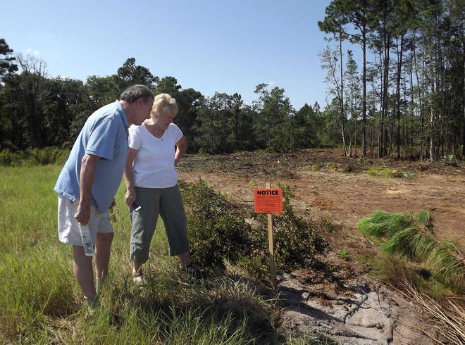 Shores residents Bruce Militello and Sue Chitwood read a sign placed by the county on an area behind their homes that was being cleared of trees. BY DOUGLAS JORDAN, Special to The Record