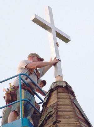 Workers from Summy Construction place the new cross atop the steeple of Holy Trinity Polish National Catholic Church.