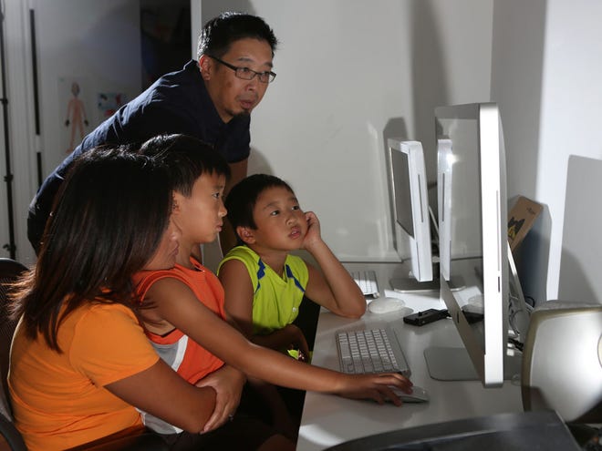 Ken and Arlyne Chin look at a reading application on the computer with their two children Col, 7, and Jackson, 8, at their home in Chicago. The parents limit the amount of time the boys can spend using the computer. (McClatchy Newspapers)