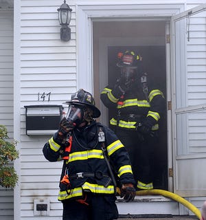 Framingham firefighters emerge from 147 Elm Street this morning after fighting a fire in the basement.