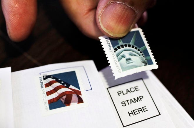 In this file photo, a customer places first class stamps on envelopes at a U.S. Post Office in San Jose, Calif. It'll cost another penny to mail a letter in 2013. The cash-strapped U.S. Postal Service said Thursday that it will raise postage rates on Jan. 27, including a 1-cent increase in the cost of first-class mail to 46 cents.
