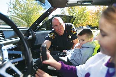 Photo by Amy Herzog/New Jersey Herald - Sheriffs Officer Warren Slahor hands the radio controller of the D.A.R.E. car to Kaitlyn Healey, 5, while her brother, Kevin Healey, 3, both of Sparta, looks on during the DASI Walk for Hope/Fun Day.