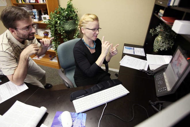 In a Sept. 27, 2012 photo, Levi Coplen, left, a deafness resource assistant, helps Heather Bise, a deafness resource specialist with Advocacy, as they work with colleague Eric Patterson, pictured on a video phone, far-right, who is based in Wichita Falls, Texas, at her office in Dallas. (AP Photo/The Dallas Morning News, Ben Torres) NO SALES; MANDATORY CREDIT; MAGS OUT; TV OUT; INTERNET USE AP MEMBERS ONLY