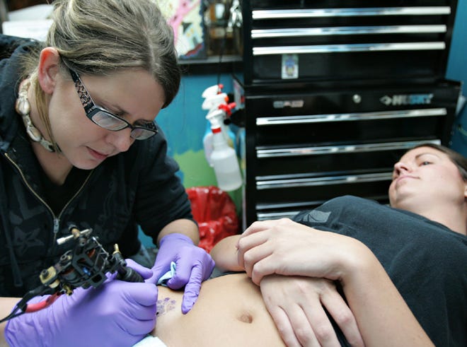 Crystal Hays, tattoo artist at Gulf Coast Professional Tattoo, tattoos a paw print onto Megan McQueen Wednesday. All paw print tattoo donations will go to the Animal Rescue Center. The print is a replica from a paw print McQueen stamped from her Chihuahua, Rufus. "I have my baby with me always," she said.
