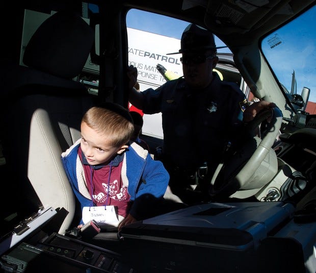 Jason Burbaugh, 5, a kindergarten student at Carlile Elementary School, gets an inside view of a Colorado State Patrol vehicle by Officer Art Gumke (back) as part of the PCC Kindercaminata. Chieftain photo John Jaques 10.19.12