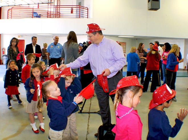 Kristian Chapman, president of local Peoples First Insurance Agency, hands out red fire helmets to kindergarten students from Holy Nativity Episcopal School on Monday.