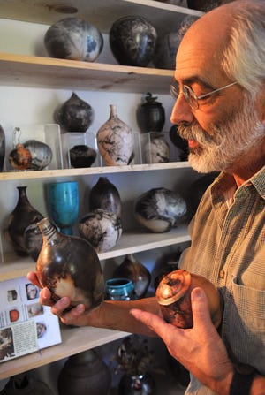 Ron Mello holds two vases he made from clay and describes the process of firing them under specific conditions to get the resulting colors on the pieces seen in his Middleboro studio on Thursday, October 11, 2012.