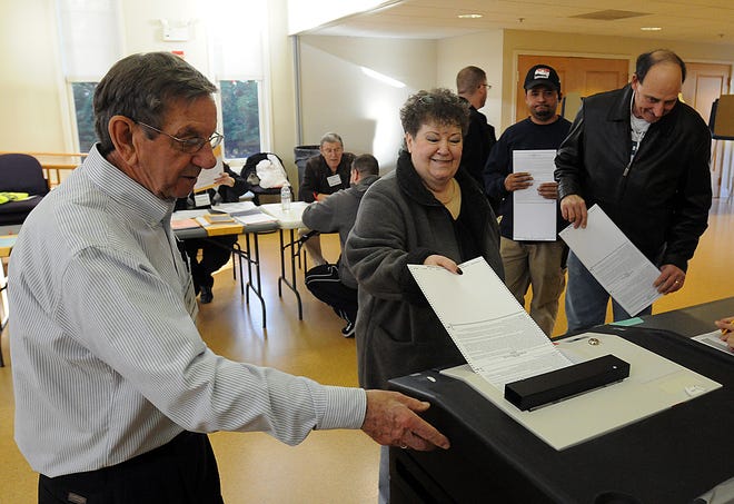 Volunteer Don Carroll watches over the ballot box as Violet Sherman casts her votes, Tuesday in Milford.
