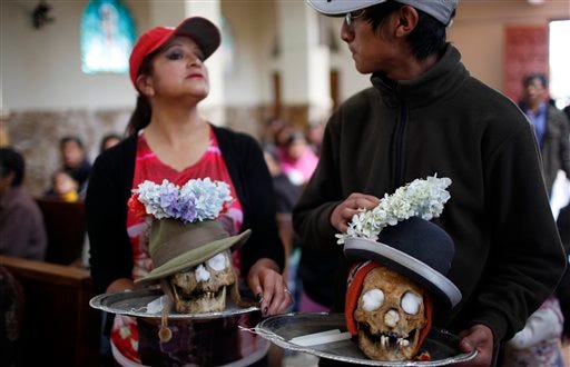 People arrive in the chapel of the Cementerio General with decorated human skulls on metal platters, to offer a prayer before attending the Natitas Festival at the largest cemetery in La Paz, Bolivia, Thursday, Nov. 8, 2012. "Natitas," are human skulls from unnamed, abandoned graves that are cared for and decorated by faithful who use them as amulets believing they serve as protection from thieves. The festival is a mixture of Andean ancestral worship rites and Catholic beliefs. According to experts, it was common practice in the pre-Hispanic era to keep skulls as trophies and display them during the rituals to symbolize death and rebirth. The festival marks the end of the All Saints’ holiday, but is not recognized by the Catholic church. (AP Photo/Juan Karita)