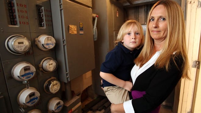 Elke Lawrence and her son, Alexander, 6, stand near Florida Power & Light meters in an electrical room outside their Flagler Yacht Club condo. Lawrence is trying to get the new meters changed back to old style meters due to health concerns.