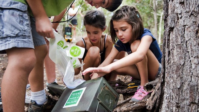 Robbie Ruiz, 7, (left) Laurel Dickerson, 10, (center) and Avery Dickerson, 7, explore the contents of a cache during a geocaching 101 class on Saturday at Buescher State Park in Smithville. Geochaching uses GPS coordinates to find stashed items, or caches, left by previous visitors.