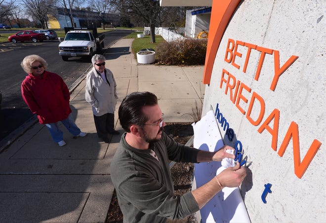 Fran Kepler left, and Hettie Beers, center, happily watch as Hardin Signs worker Gerry Skalla drills holes to install the lettering and signs on a tribute monument to Peoria's Betty Friedan Friday outside of the former YWCA. Last June, the building was put up for auction and the monument was stripped bare of the tribute lettering.