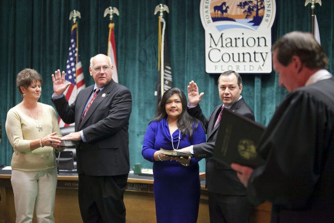 From left, Shelia Arnett stands with her husband new commissioner Earl Arnett and Loida Moore stands with her husband new Commissioner David Moore as Judge David Eddy performs the swearing in ceremony at the Marion County Commissioners meeting at the McPherson Complex in Ocala on Tuesday.