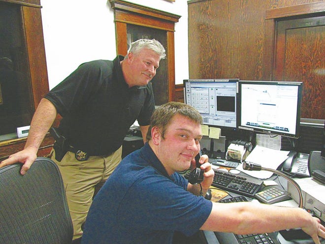 Yreka Police Department's (YPD) new dispatcher Seth Fortna-Hanson sits at the department's dispatch center as YPD Chief Brian Bowles looks on.