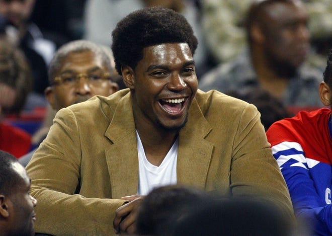 Sixers center Andrew Bynum laughs as he watches a preseason game against the Brooklyn Nets.