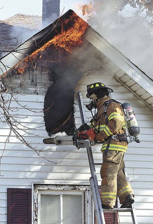 John Gaines/The Hawk Eye A Burlington firefighter saws open the attic while battling a blaze that gutted the house at 811 Sycamore St. Friday in Burlington.