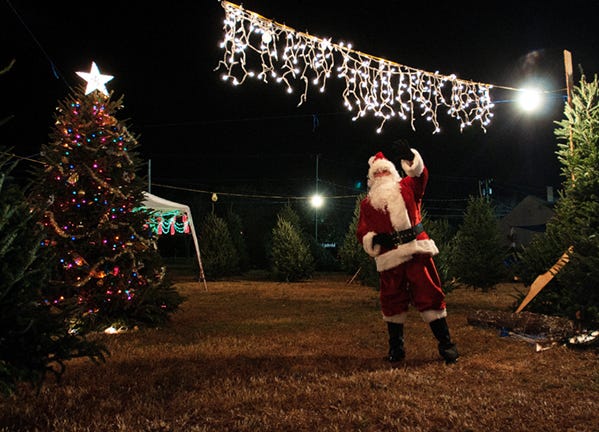 Santa Claus waves Friday night from the Reagan Bunch Christmas Tree Lot beside Hayes Jewelers on Ninth Street. The Bunch family sells only 30-year-old trees from their farm in White Top Mountain, Va. for $35-50 each.