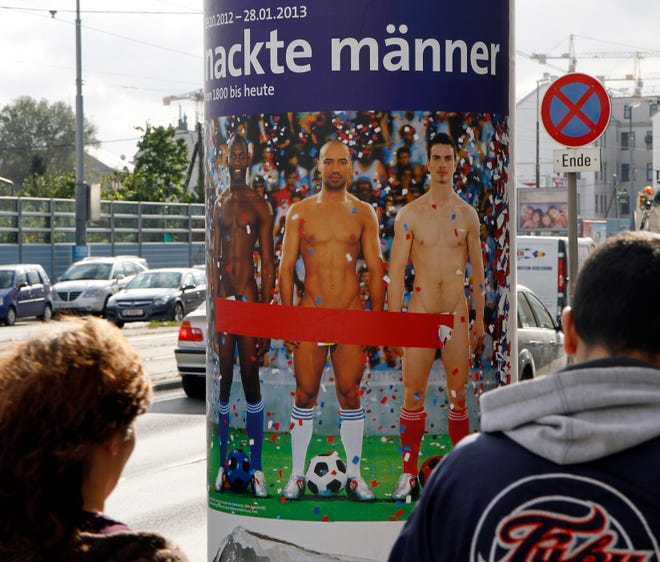 In this Oct. 18, 2012 file photo two people walk past a poster showing three naked men which has had red tape added to cover the sensitive parts of the three men, in Vienna, Austria. Poster reads: "Naked Men". A prestigious Vienna museum, The Leopold Museum, says a man took the concept of life imitating art to an extreme recently when he suddenly stripped at an exhibition of pictures and sculptures portraying nude men through the ages. A museum spokesman said Tuesday Dec. 11, 2012 that after taking his clothes off, the man calmly sauntered through the exhibition, dressing again only after a security guard asked him to do so. (AP Photo/Ronald Zak, File)
