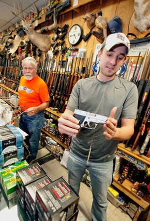 Dan Barth of Pekin Gun and Sporting Goods shows a Kahr 9mm concealable handgun as Craig Salmon looks on Tuesday evening. Barth described the brisk business in the store as normal for a weekday.