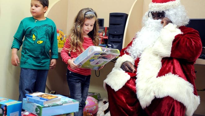 Henry Miller, dressed as Santa, watches Jason Hernandez, 8, and Ava Artlip, 5, choose gifts during a holiday party at the South Olive Community Center on Friday.