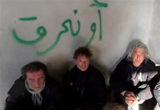 This image taken from undated amateur video posted on the Internet shows NBC chief foreign correspondent Richard Engel, center, with NBC Turkey reporter Aziz Akyavas, left, and NBC photographer John Kooistra, right, after they were taken hostage in Syria. More than a dozen heavily armed gunmen kidnapped and held Engel and several colleagues for five days inside Syria, keeping them blindfolded and tied up before they finally escaped unharmed during a firefight between their captors and anti-regime rebels, Engel said Tuesday, Dec. 18, 2012. The Arabic writing on the wall reads, "or we will burn."(AP Photo/Amateur Video)