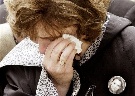 In this June 7, 2002 file photo, Beth Nimmo, with a button bearing a photo of her daughter Rachel Scott who was killed at the Columbine High School shooting, wipes her eyes at the Gutenberg High School, where a 19-year-old former student shot 16 people before killing himself in Erfurt, eastern Germany.