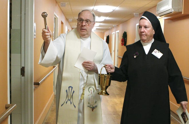 Giving the recently completed construction a solemn blessing, The Reverend Peter Gojuk O.M.V., left, sprinkles holy water at the doorway of a room that will be used by a future patient at St. Patrick’s Manor, during the dedication of the new wing on Monday afternoon. Sister Mary Brigid Riley, O. Carm. holds the holy water for the ceremony. Sister Mary Brigid is the chaplain for the Carmelite Sisters who provide patient care at St. Patrick’s Manor.