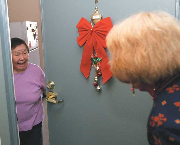 Photo by Tracy Klimek/New Jersey Herald - Liberty Towers resident Sumi Matthies smiles Wednesday, Dec. 19, as she opens the door to her apartment to Elenora Benz, who delivered her Earth Angels package.