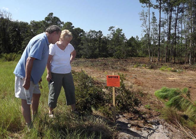 Shores residents Bruce Militello and Sue Chitwood read a sign placed by the county on an area behind their homes that was being cleared of trees. By DOUGLAS JORDAN, Special to The Record