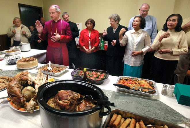Springfield Catholic Bishop Thomas John Paprocki blesses food, part of a feast in the Sacred Heart Church parish center, during Simbang Gabi on the evening of Sunday, Dec. 23, 2012. Bishop Paprocki had earlier celebrated the final Simbang Gabi Mass along with members of the Springfield Filipino community who stand with him during the blessing. Traditional Filipino, Spanish and Chinese dishes made up the food dishes.