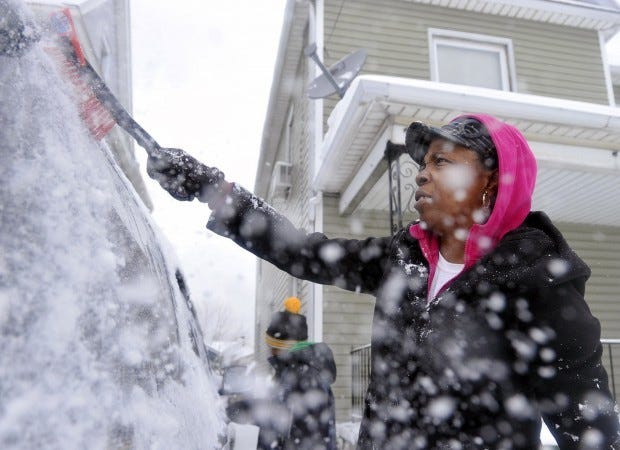 Ice and snow fly as Cornelia Beard, right, and her son, Keshaun Beard, 8, background left, both of Erie, clear snow off of their car Thursday after a winter storm dumped 9 inches of snow in the Erie region, according to the National Weather Service.