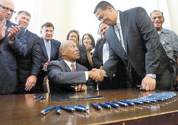 Massachusetts Gov. Deval Patrick, center, shakes hands with Cedric Cromwell, chairman of the Mashpee Wampanoag tribe, right, moments after Patrick signed a casino compact bill during ceremonies at the Statehouse, in Boston on July 30.