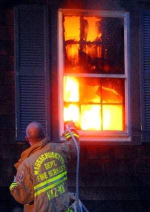 Bourne Deputy Fire Chief Joe Carrara places a garden hose through a window at the scene of a house fire on Portside Drive in Bourne Monday afternoon before engine companies arrived on scene.