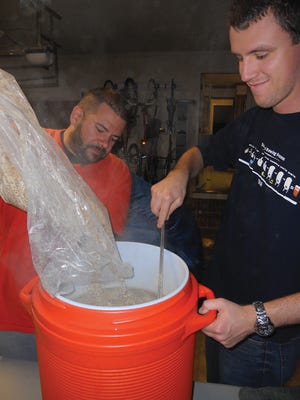 Ricardo Ramirez, left, and Ian Baltutis add malt to boiled water in a homemade mash tun last month at the last East of Elon Home Brewing Cooperative meeting of 2012. Ramirez strained the mixture and was left with “wort,” to which hops was added during another boil. The IPA-style beet will ferment and be ready to drink in four to six weeks.