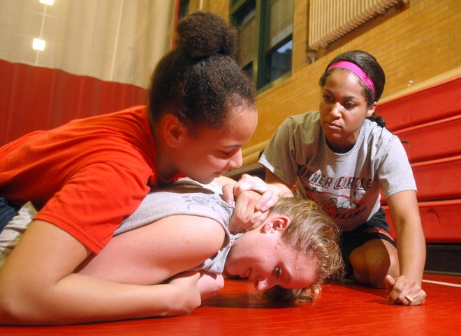 Assistant Coach Jade Perry works with freshman Kiara Clairborne 14, in red and junior Margaret McDonough 18, on techniques during practice. NFA has 20 girls this season that makes up part of this years NFA Wrestling team.