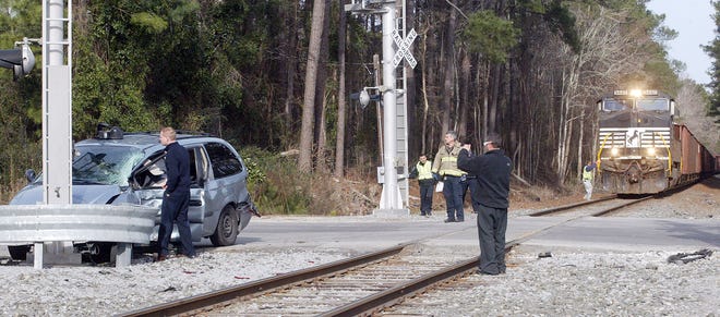 Co-workers and friends of a woman who drove her van into the path of a Norfolk-Southern train look at the scene Friday at the crossing at Greenfield Heights Boulevard in Havelock. After the collision, the train backed up down the tracks to clear the crossing for traffic. The woman, Sharon Ann Tull, of Havelock, was treated and released from the hospital but faces multiple charges in connection with the crash.