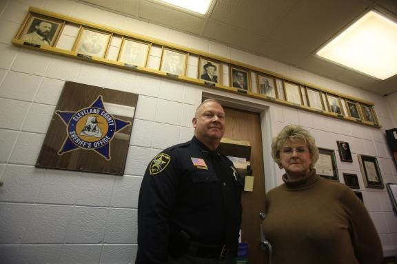 Sheriff Alan Norman and administrative assistant Millie Snyder pose in front of the current display of former sheriffs. Nine photos are missing. If you have a photo of one of the county's past sheriffs, contact Snyder at 704-484-4817.
